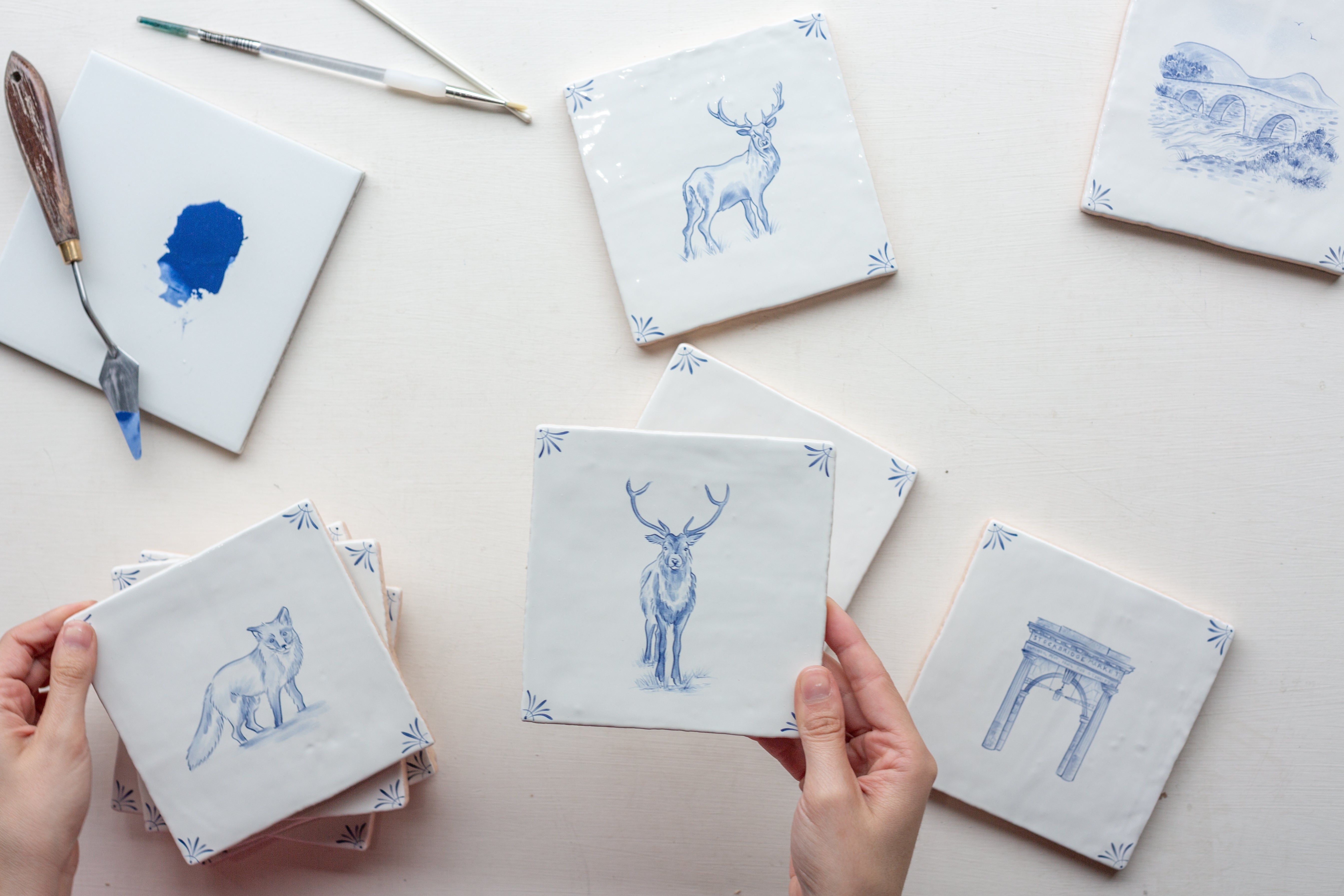 Hands holding ceramic tiles in a delft blue style. Tiles of animals and architecture.