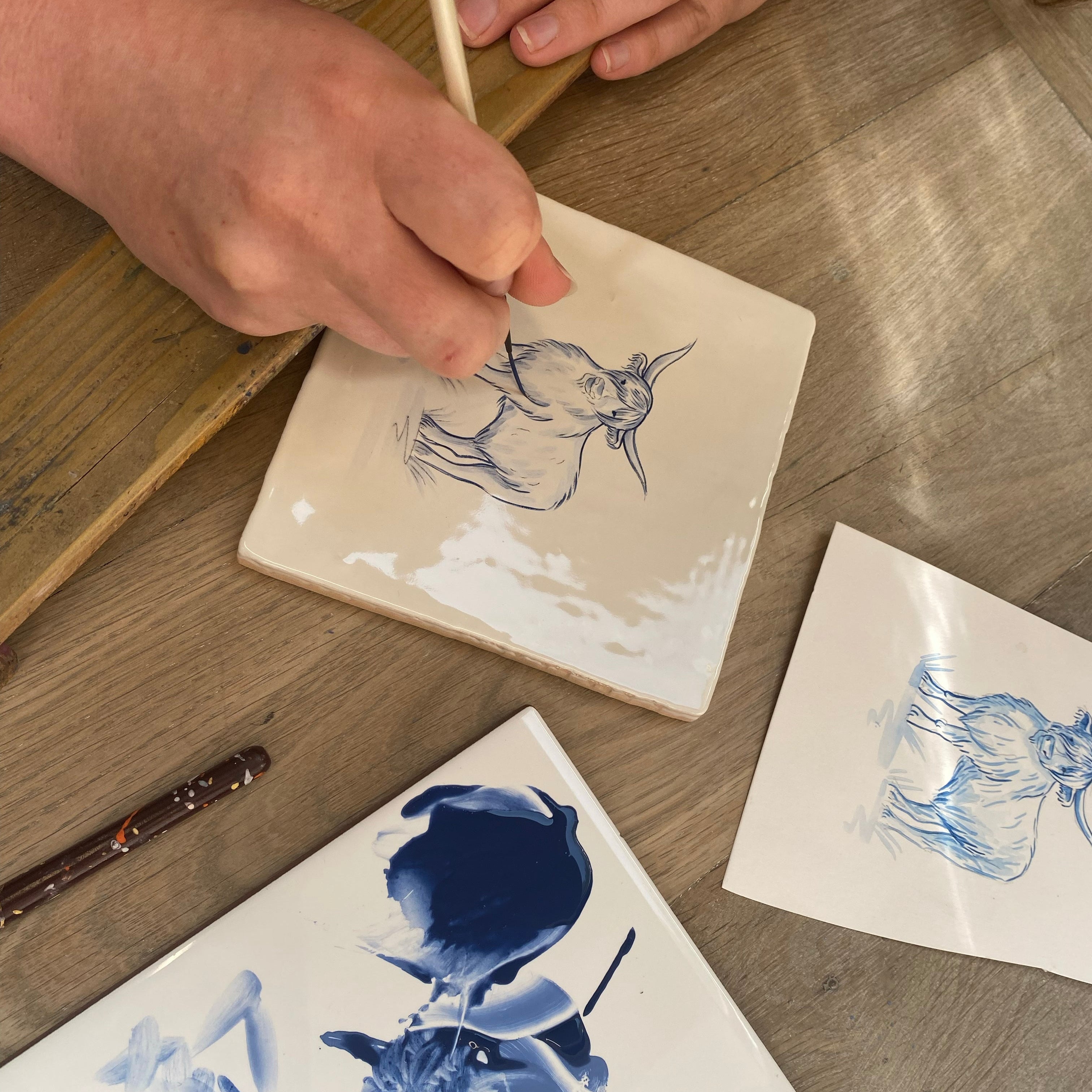 Person painting delft style animal on ceramic tiles with a brush.
