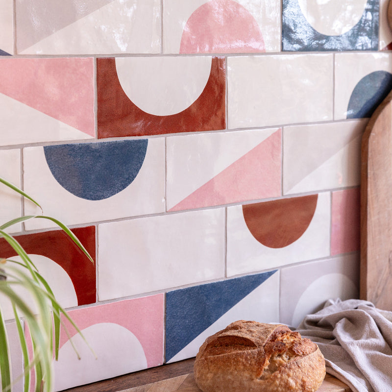Colorful geometric-patterned tiles on a wall with a loaf of bread and a plant in the foreground.