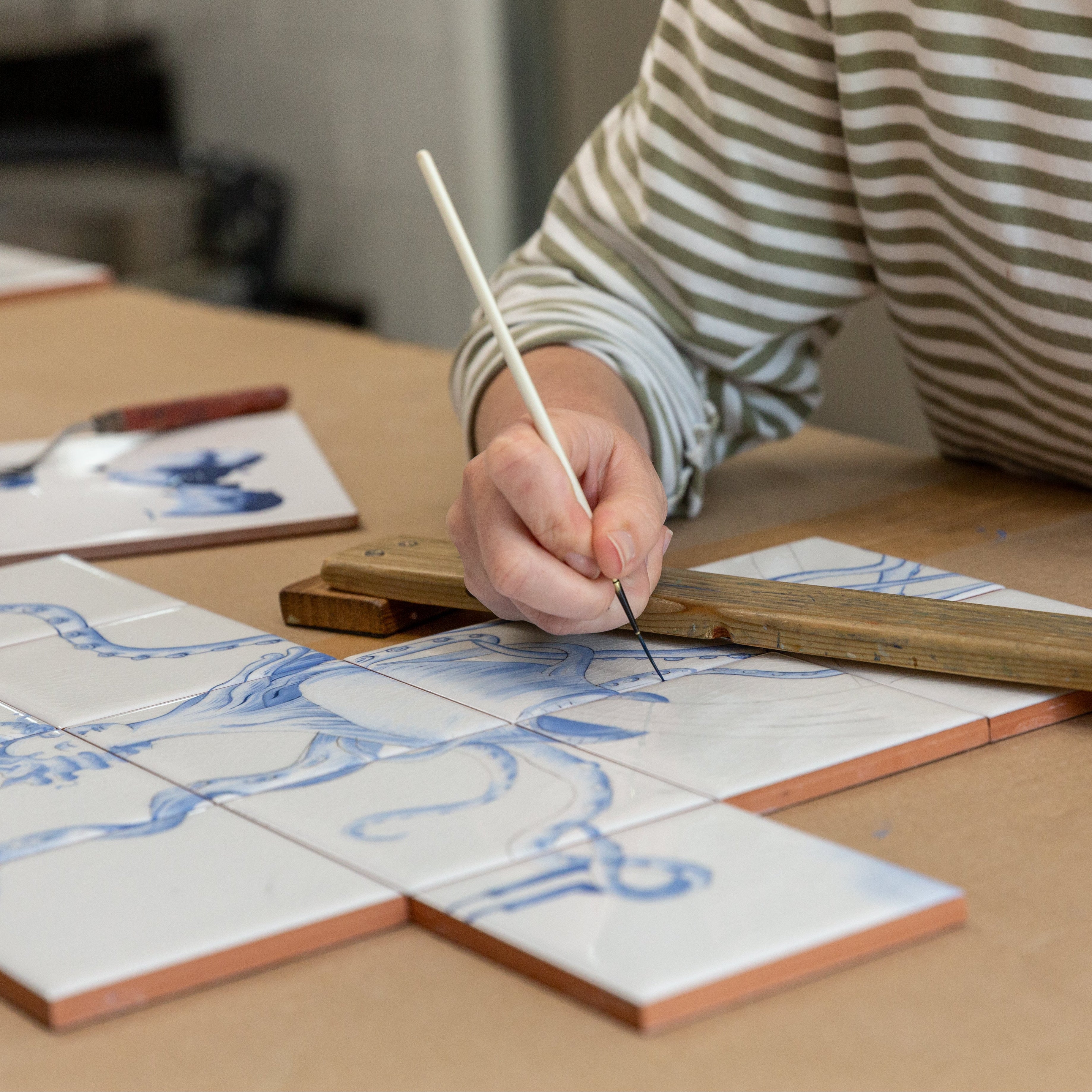 Person working on a ceramic tile design with a brush