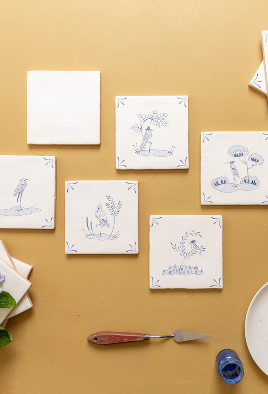 Decorative tiles with blue delft designs on a beige surface, accompanied by a paintbrush and container.